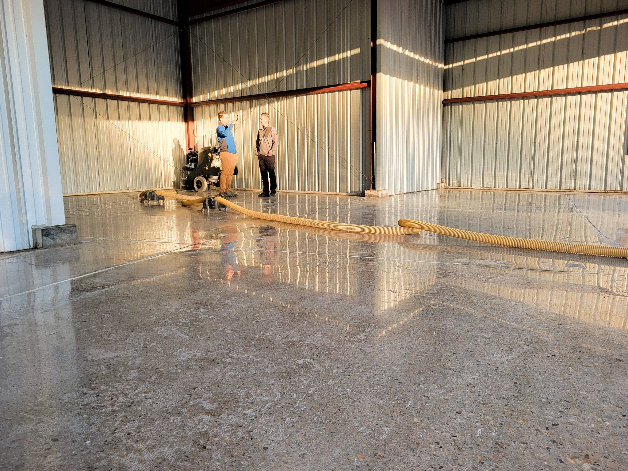 The 8KR working across a large warehouse floor, its yellow vacuum hose trailing behind