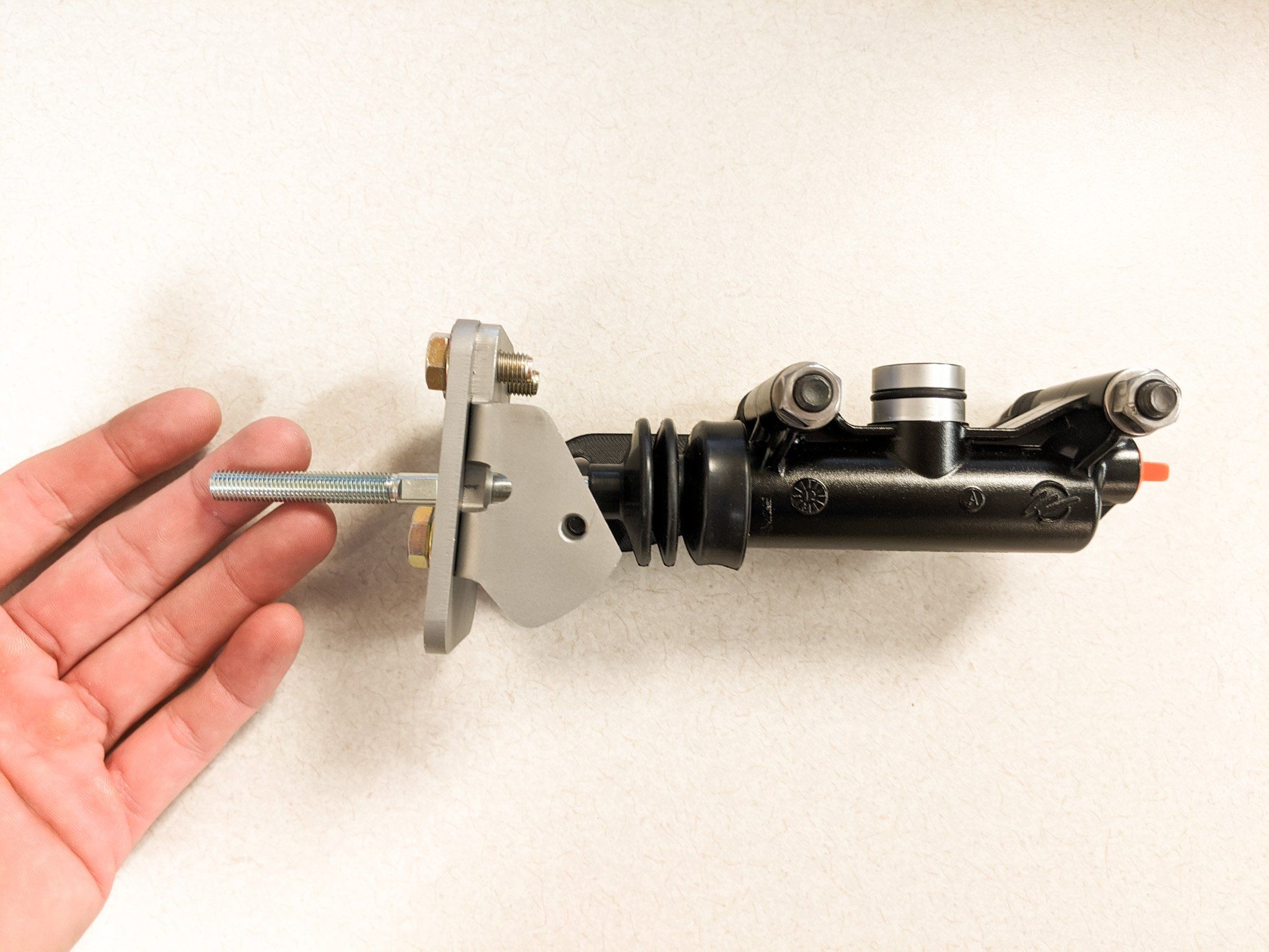 The assembled bracket and master cylinder in an open hand, to show its size