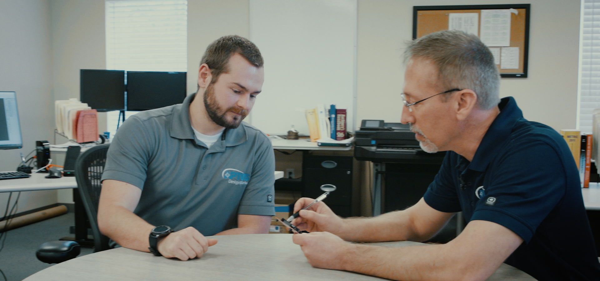 Two APTUS engineers talking through a part at the table