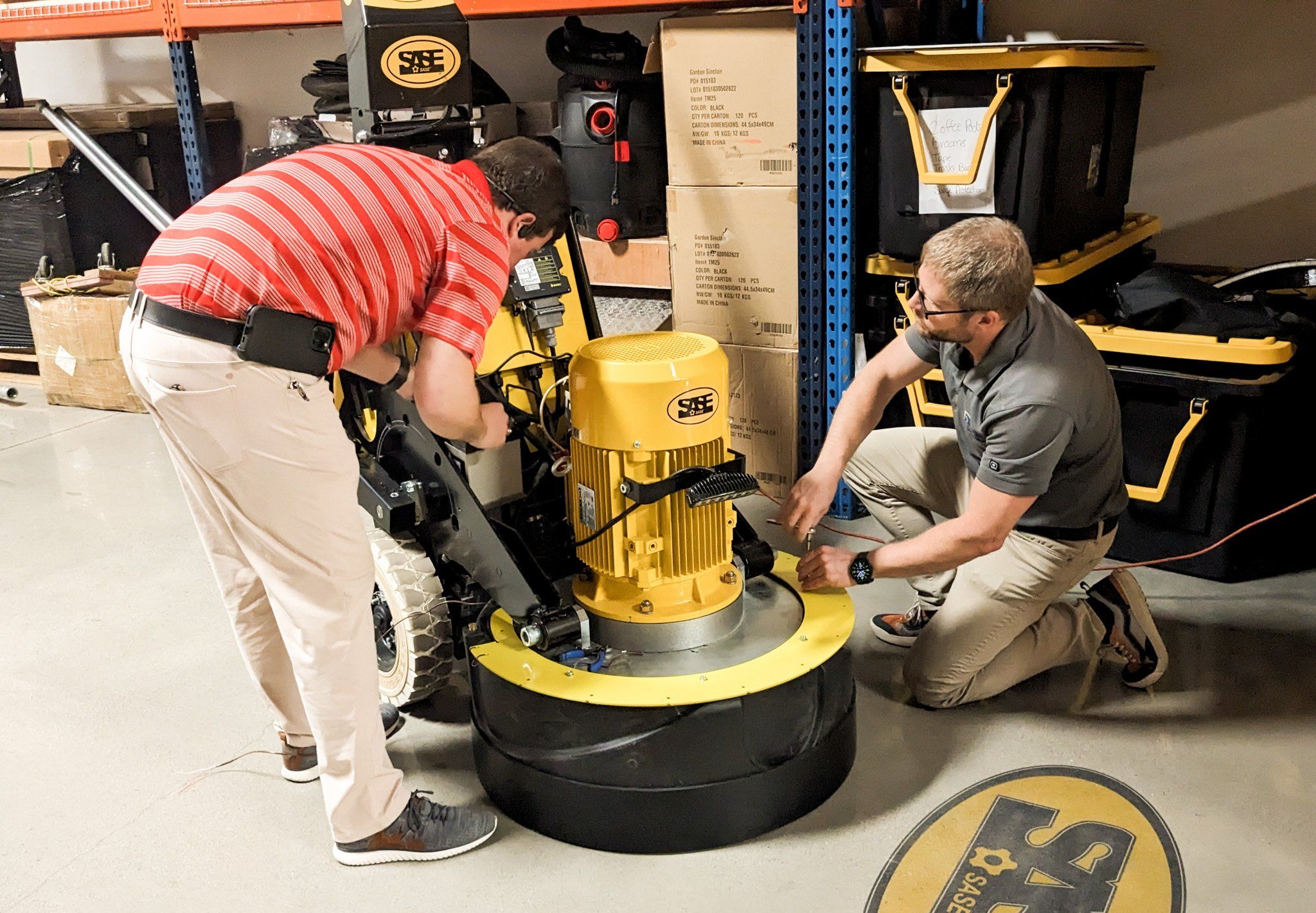 Two APTUS engineers working on a yellow SASE grinder in the shop